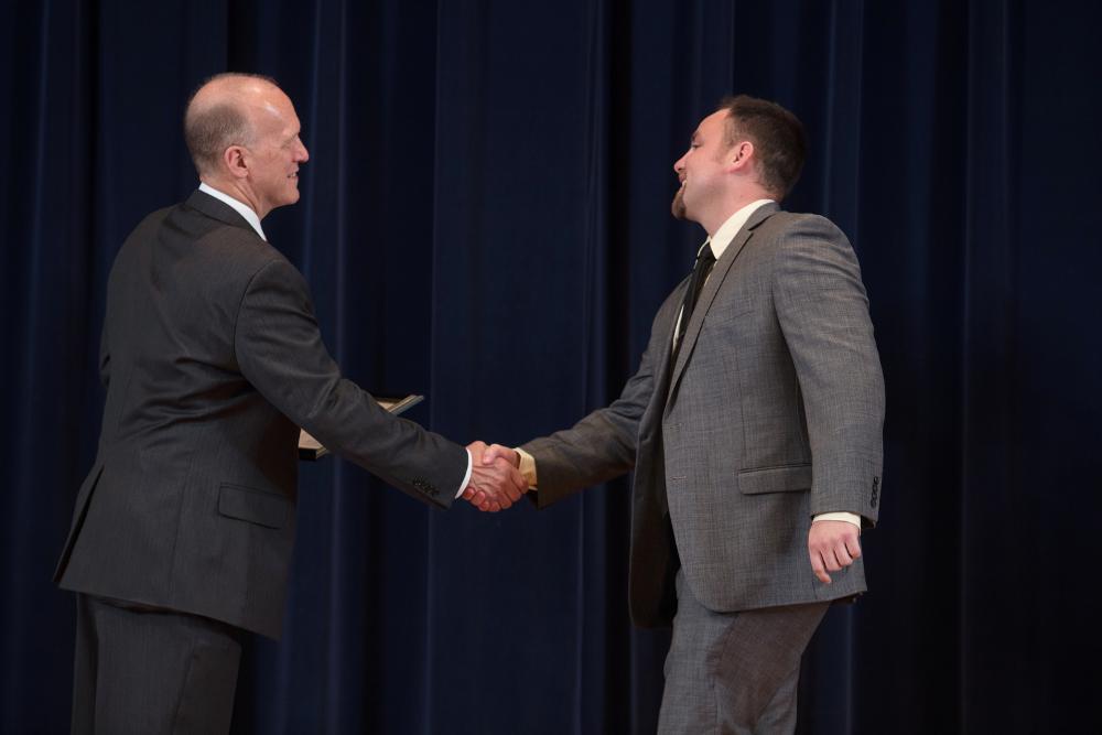 Doctor Potteiger shaking hands with an award recipient in a grey suit and black tie